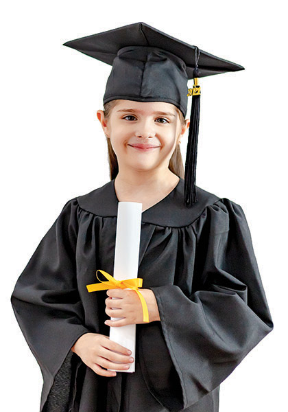 A young girl is wearing a black graduation cap and gown. She is smiling and holding a rolled-up diploma tied with a yellow ribbon.