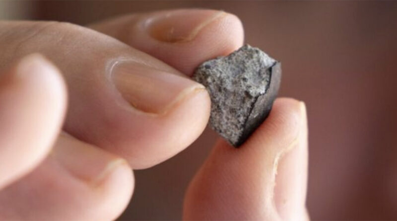 A small gray rock, about the size of a fingernail, is being held between two fingers. It’s rough and jagged and looks like it came from outer space.
