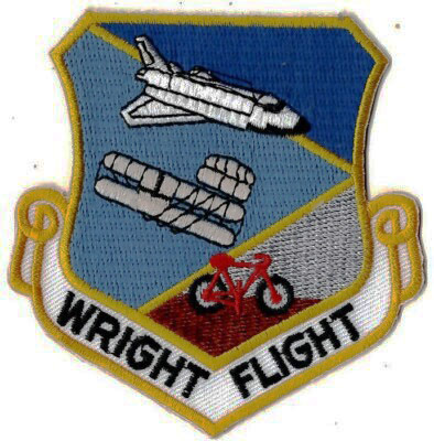 A military-style patch showing a space shuttle, Wright Flyer plane, and bicycle with "WRIGHT FLIGHT" text.
