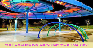 Colorful splash pad at night with glowing rainbow lights and curved water arches, under a large modern shade structure.