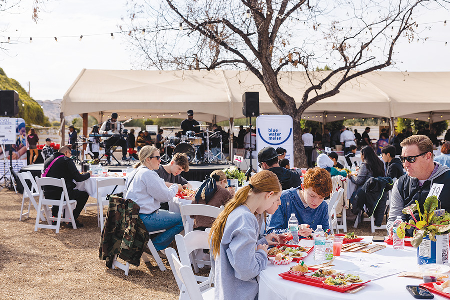 People are eating lunch at outdoor tables while a band plays music on stage under a big tent.