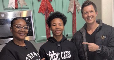 Three people smile for a photo in a kitchen. Two wear black shirts and one wears a hoodie that says "I AM TRENT CARES."