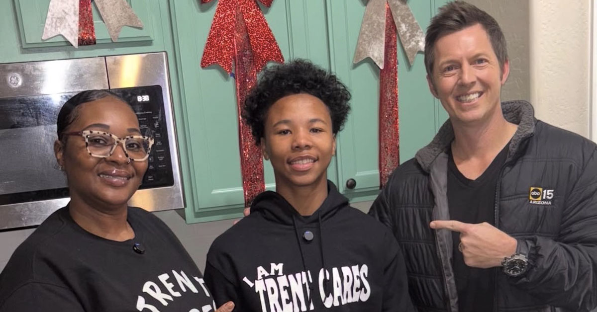Three people smile for a photo in a kitchen. Two wear black shirts and one wears a hoodie that says "I AM TRENT CARES."