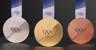 Three shiny Olympic medals—gold, silver, and bronze—hang side by side with ribbons and the Olympic rings on them.