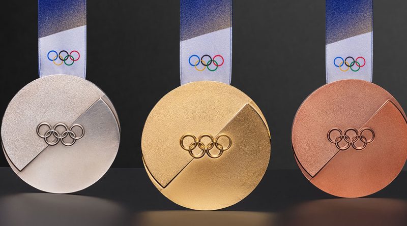 Three shiny Olympic medals—gold, silver, and bronze—hang side by side with ribbons and the Olympic rings on them.
