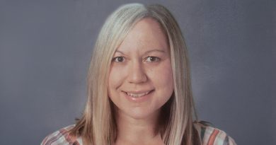 Smiling woman with long blonde hair wearing a striped shirt, photographed against a gray background in a professional headshot.