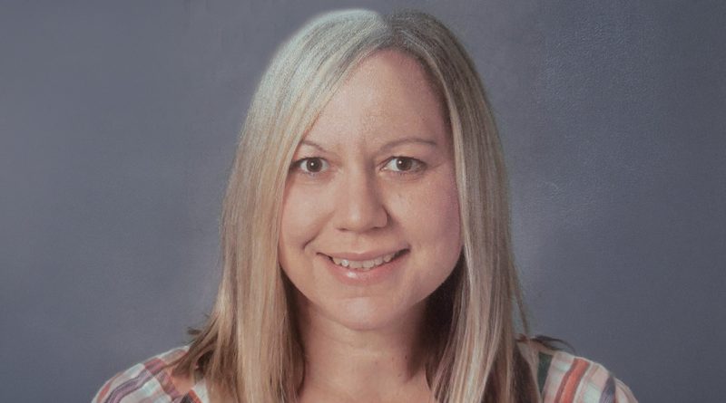 Smiling woman with long blonde hair wearing a striped shirt, photographed against a gray background in a professional headshot.