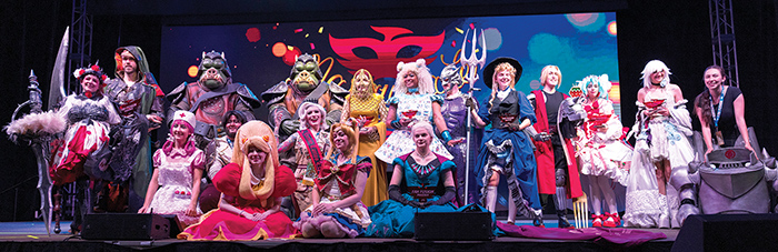 Large group of people on stage wearing colorful costumes and wigs from movies, comics, and video games at a cosplay comic book convention.