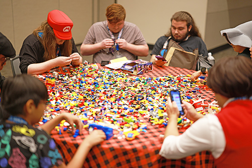 People sitting around a table covered with thousands of colorful LEGO bricks, building different creations together.