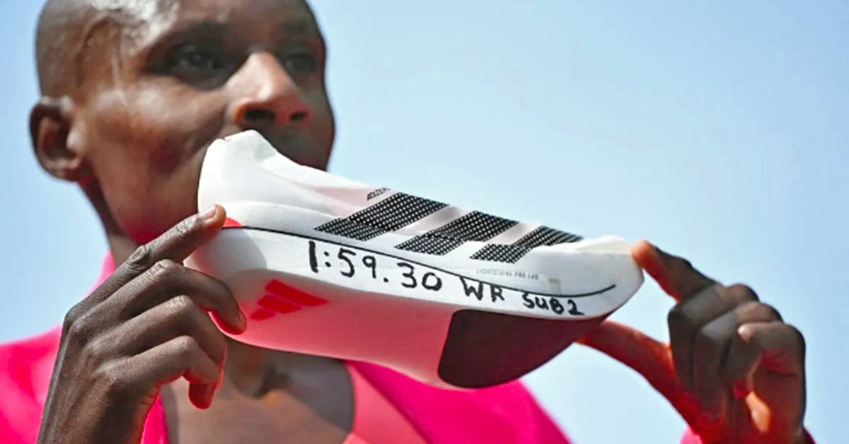 Runner wearing pink holds up a white running shoe with black stripes and "1:59.30 WR SUB2" written on the bottom in marker.