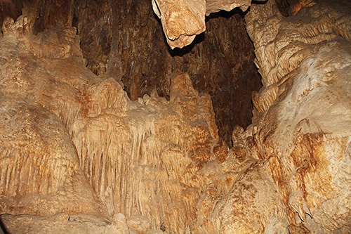 Inside a large cave with tall stalactites hanging from the ceiling and stalagmites rising from the floor, lit by warm golden lights.
