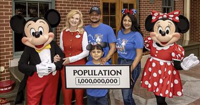 A family poses with Mickey and Minnie Mouse at Disneyland holding a sign that reads 'Population 1,000,000,000.