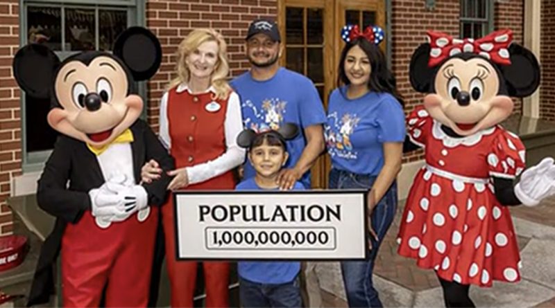A family poses with Mickey and Minnie Mouse at Disneyland holding a sign that reads 'Population 1,000,000,000.
