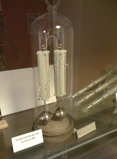 A glass dome display case containing an old scientific instrument called a Demonstration Dry Pile, purchased in 1840.