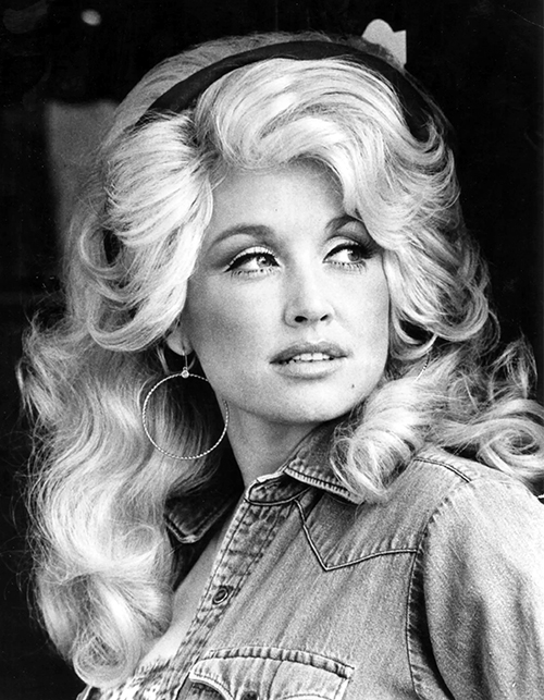 Black and white photo of a Dolly Parton with big, voluminous curly blonde hair and large hoop earrings, looking to the side.